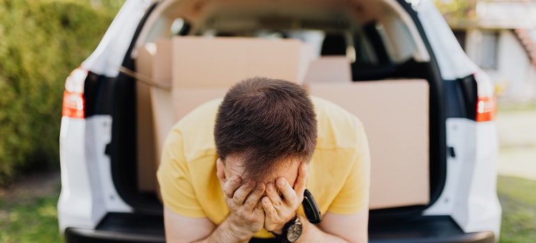 Man covering face with hands near car trunk